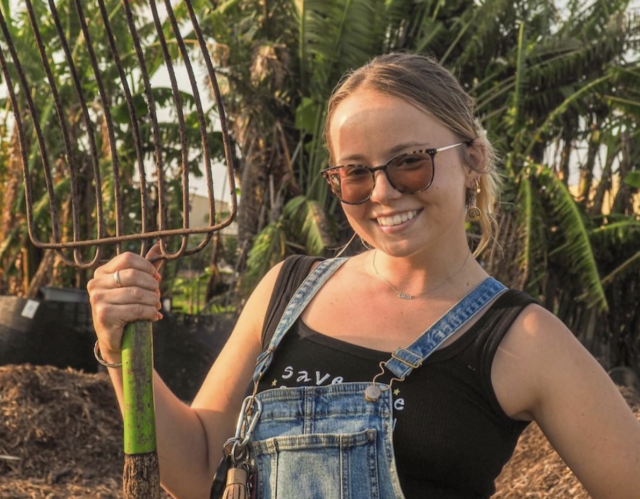 person standing with a pitchfork in front of compost area